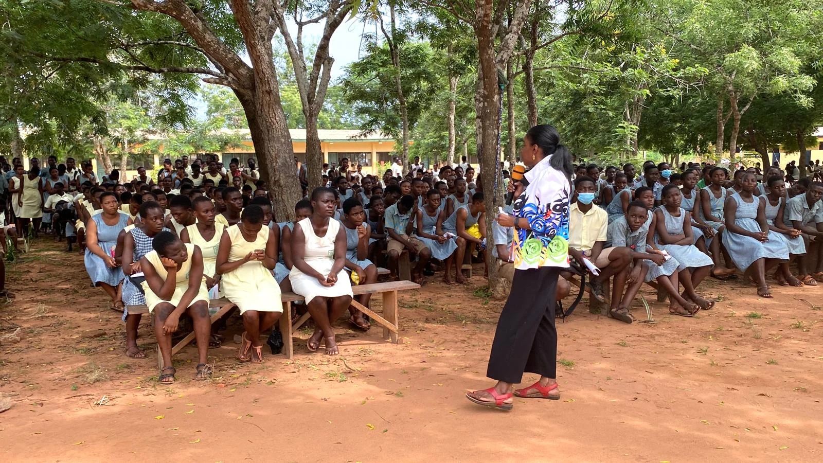 A speaker addressing students gathered outdoors beneath the trees